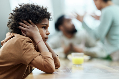 frustrated child with parents fighting in the background