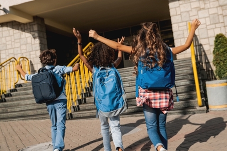 Group of happy multiracial schoolmates elementary middle school kids pupils walking to school together running hurrying to the building for classes lessons. Welcome back to school