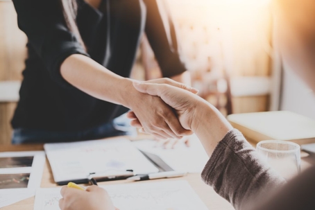Two people shake hands over a desk covered with divorce paperwork.